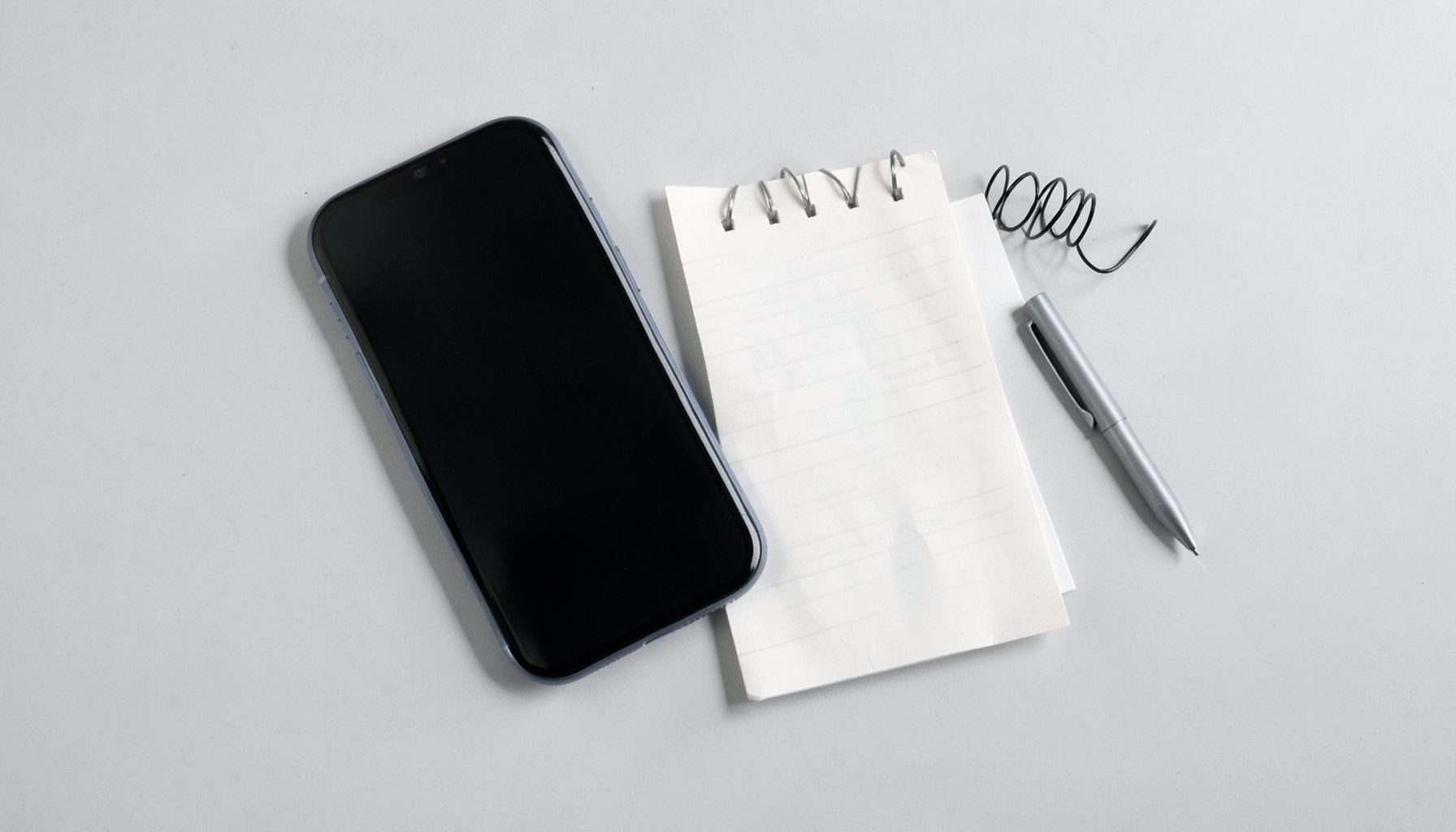 Smartphone and notepad on a light grey desk, suggesting technology topics