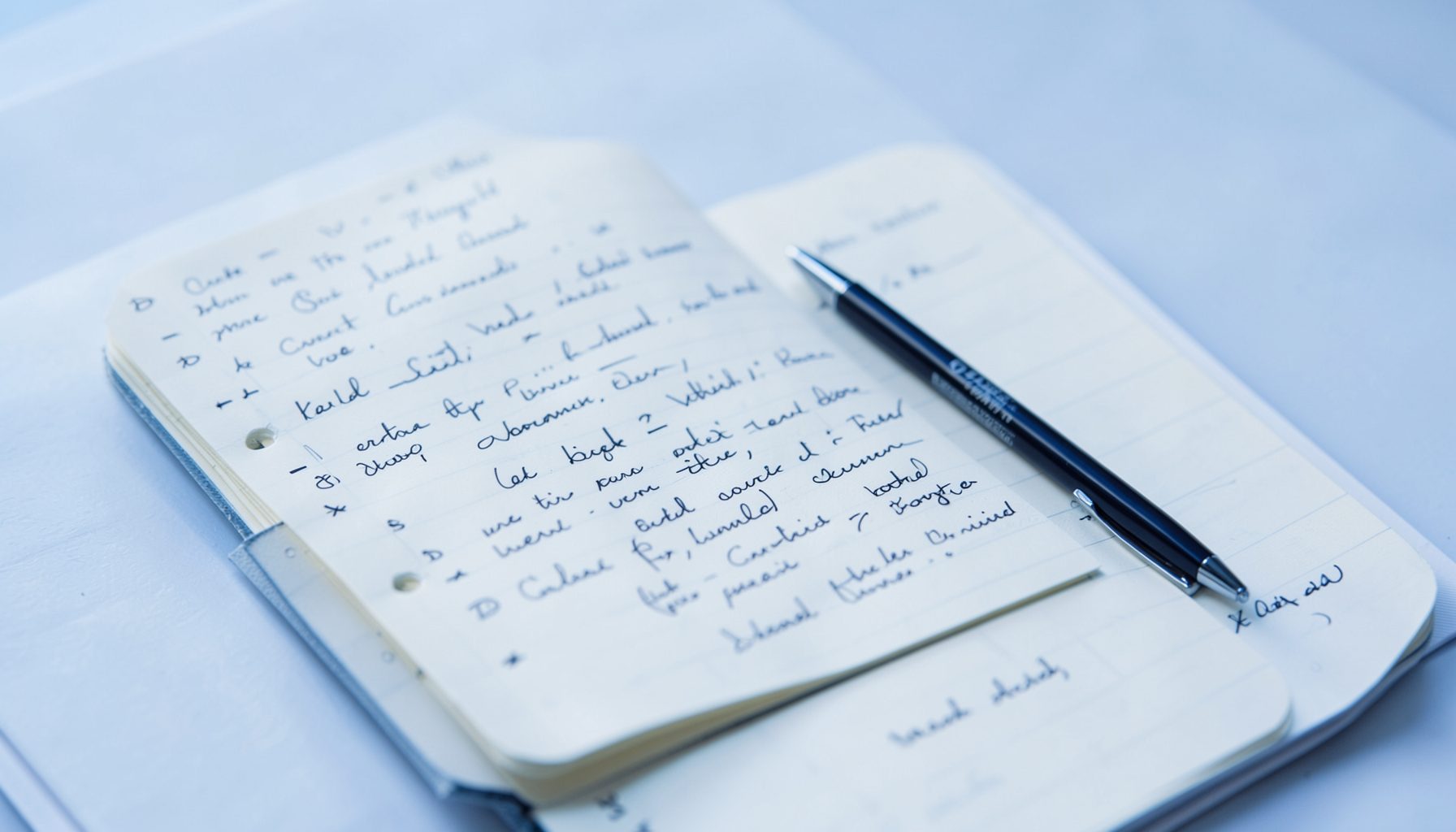 Open notebook with handwritten notes and a pen on a desk, bathed in soft daylight with calm blue and white tones